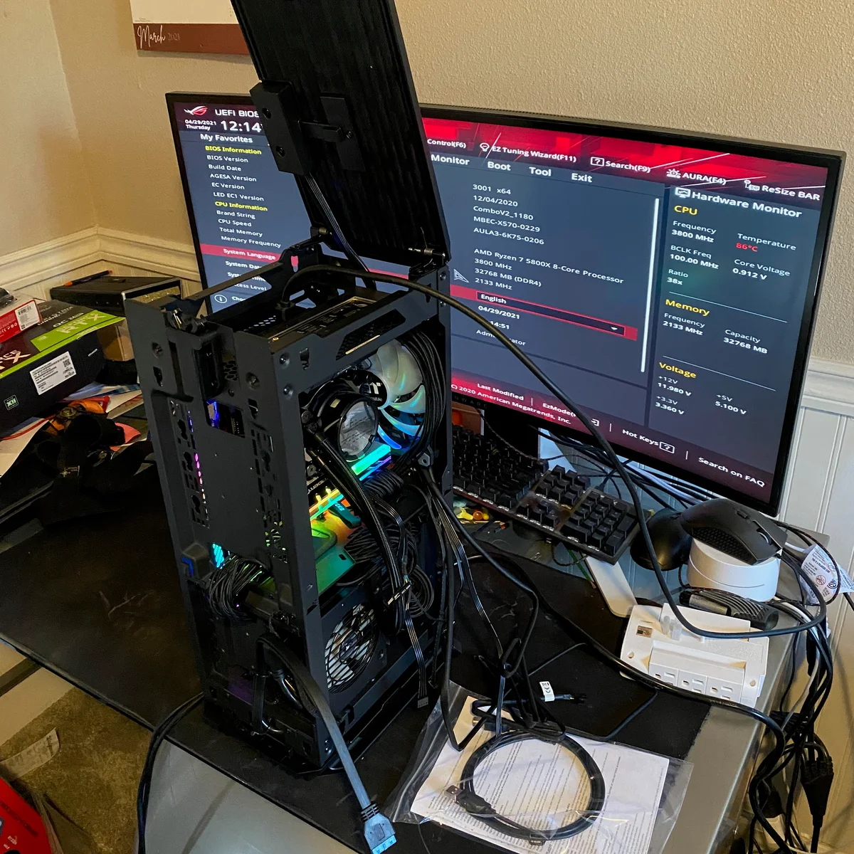 Custom PC undergoing testing beside a monitor displaying its BIOS settings